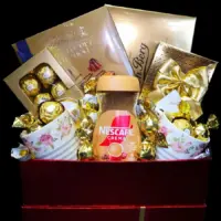 Poklon set Nes Gold sa Nescafé Crema kafom, dve cvetne šolje i čokoladnim poslasticama u bordo ukrasnoj kutiji
